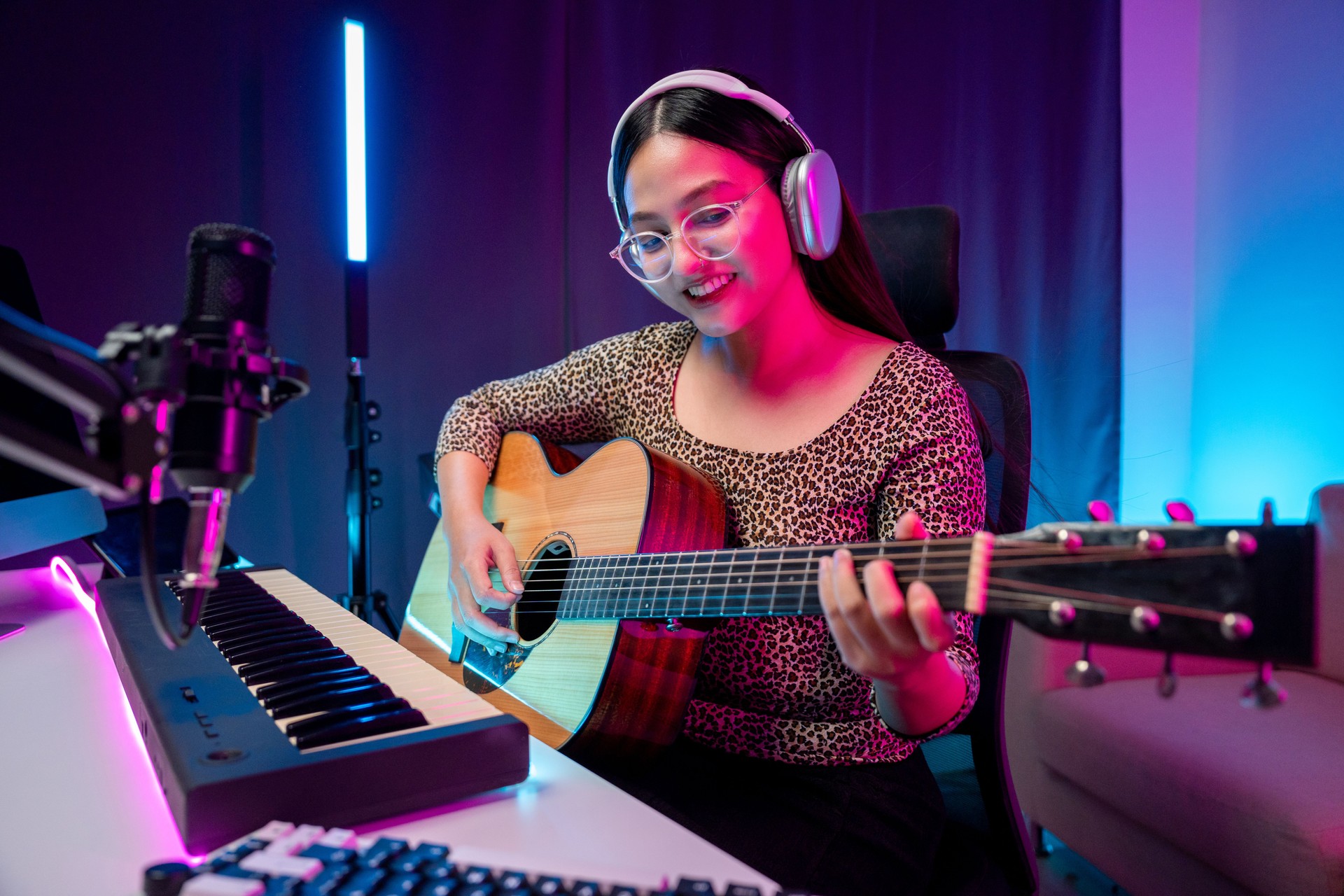 Professional Musician with condenser microphone and tablet for Mixing Mastering music. Music composer woman composing a song with guitar and piano keyboard at digital Recording home studio neon light